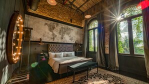 Un dormitorio con una cama grande, un banco, un mapa del mundo en la pared y vistas a la vegetación a través de la ventana.