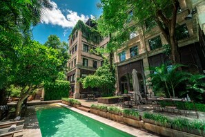 A poolside area with outdoor seating, a pool, and a building with brick walls and large windows. - Factoria Hotel (Asunción)