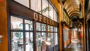 Un pasillo con un restaurante llamado "OELIA" a la izquierda, con amplias ventanas y un suelo de baldosas con diseños decorativos.