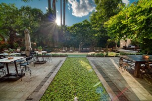 Un patio al aire libre con mesas y sillas, una fuente central y abundante vegetación.