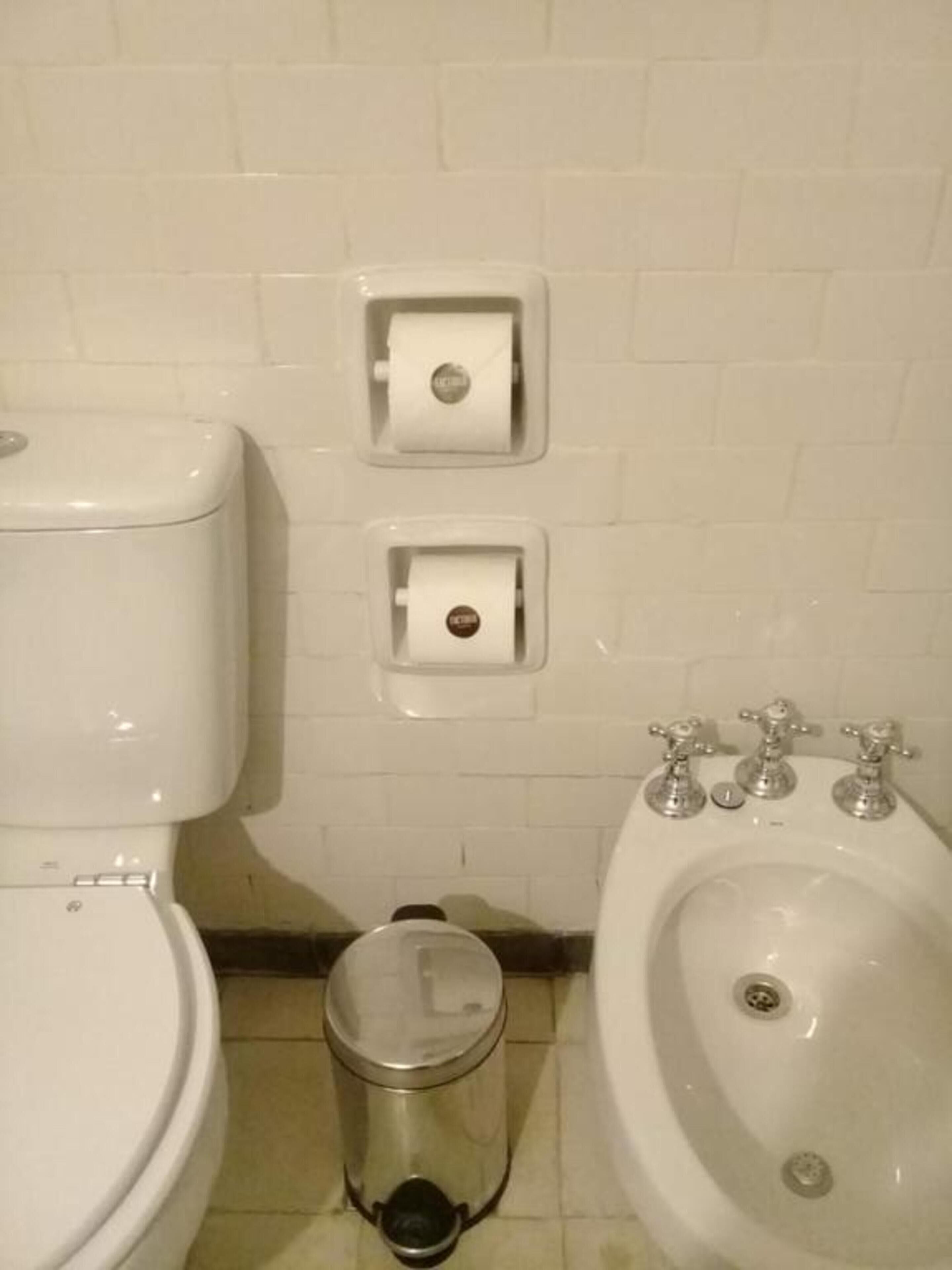 Un baño con inodoro, bidé y cubo de basura.