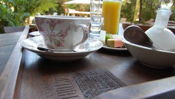 Une table en bois sur laquelle se trouvent une tasse et une soucoupe à motifs floraux, un verre de jus d’orange, un bol avec une cuillère et une bouteille de lait.