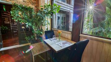 Un comedor con una mesa dispuesta para dos, una planta en maceta y una ventana con vista a follaje.
