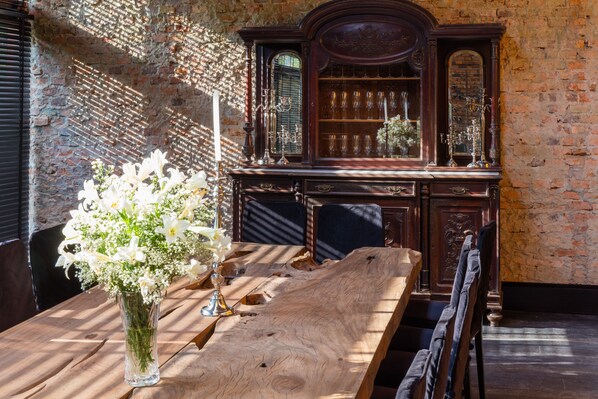 A wooden table with a vase of white flowers, a mirror, and a dark wooden cabinet with glass doors. - Factoria Hotel (Asunción)