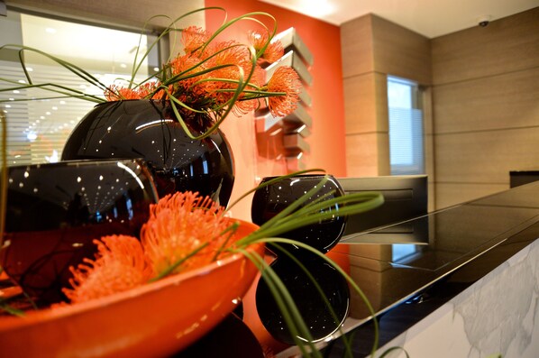 Une cuisine moderne avec un plan de travail noir, un grand saladier orange et un vase noir orné de fleurs oranges.