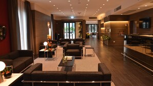 A modern hotel lobby with a seating area, a reception desk, and a kitchen area. - Hotel Forum (Baranzate)