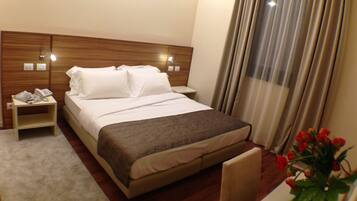 A hotel room with a wooden headboard, a bed with white linens, a bedside table with a telephone, and a vase with red flowers.