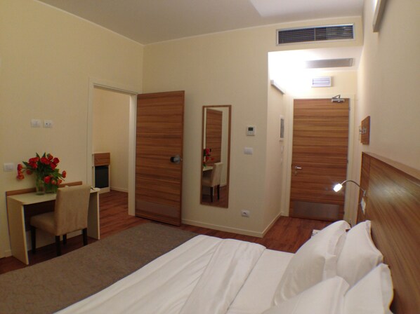 A hotel room with a bed, a desk with a chair, a mirror, and a bathroom door. - Hotel Forum (Baranzate)