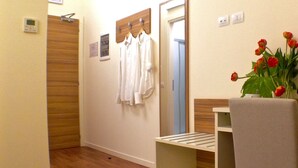 A hotel room with a wooden floor, a white chair, a small table, a mirror, and a vase with red flowers. - Hotel Forum (Baranzate)