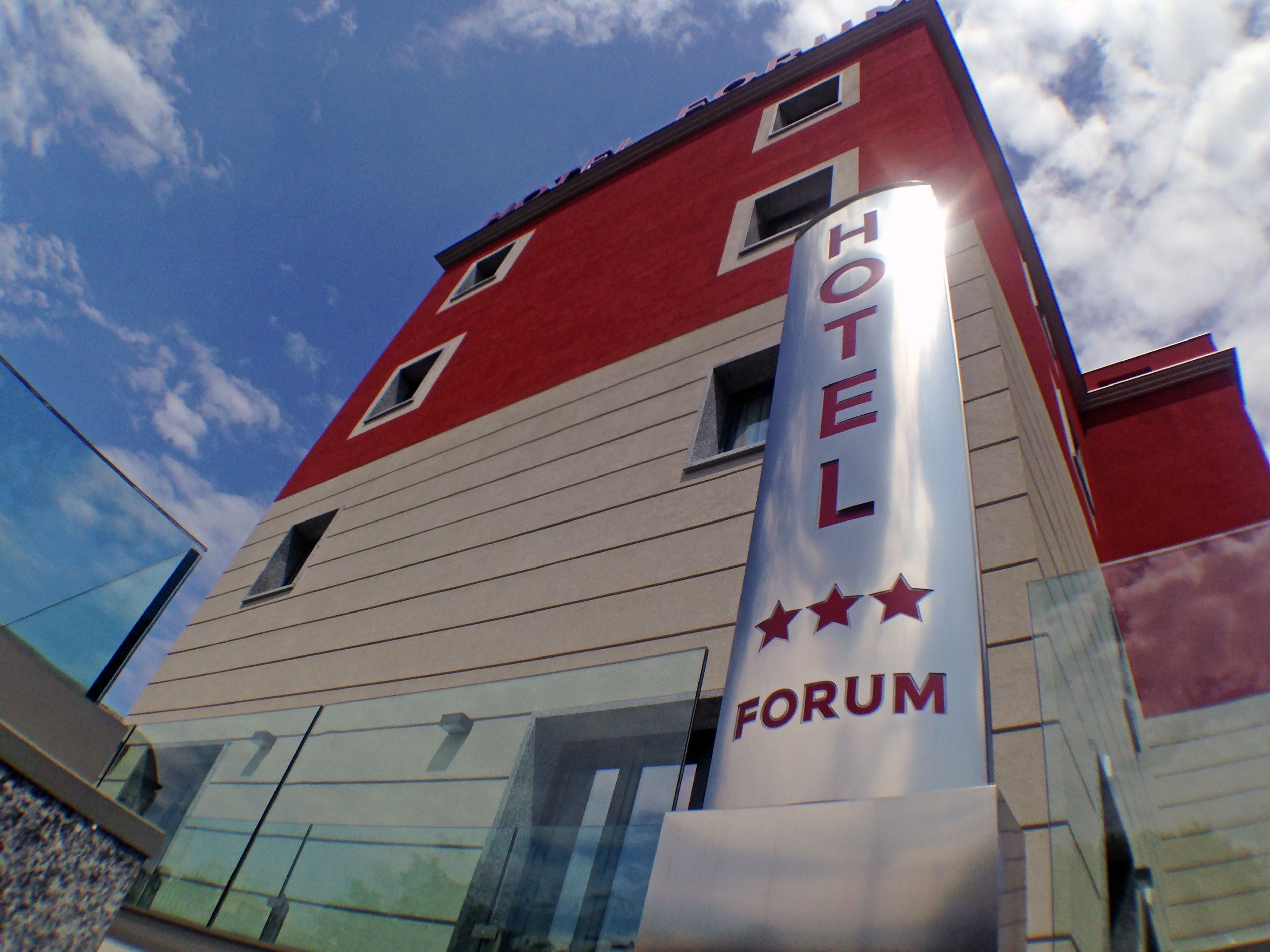 Un hotel con fachada roja y blanca, un letrero llamativo que dice "HOTEL FORUM" y tres estrellas que indican su categoría.