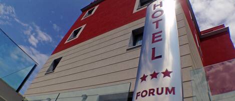 Un hotel con fachada roja y blanca, un letrero llamativo que dice "HOTEL FORUM" y tres estrellas que indican su categoría.
