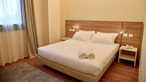 A neatly made bed with white linens and two rolled towels, a bedside table with a phone, and a wall-mounted light fixture. - Hotel Forum (Baranzate)