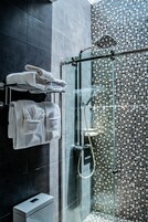 Un baño moderno con ducha envuelta en vidrio, un perchero con toallas dobladas y un muro con mosaico de azulejos.