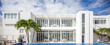 Una casa moderna de dos pisos con piscina, ventanas amplias y mobiliario exterior.