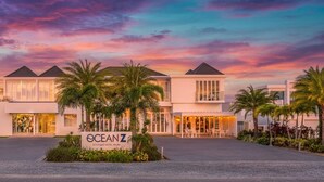 Ein stilvolles Boutique-Hotel mit modernem Design, das eine große Eingangshalle, Palmen und ein Schild mit der Aufschrift 'OCEANZ Boutique Hotel Aruba' zeigt.