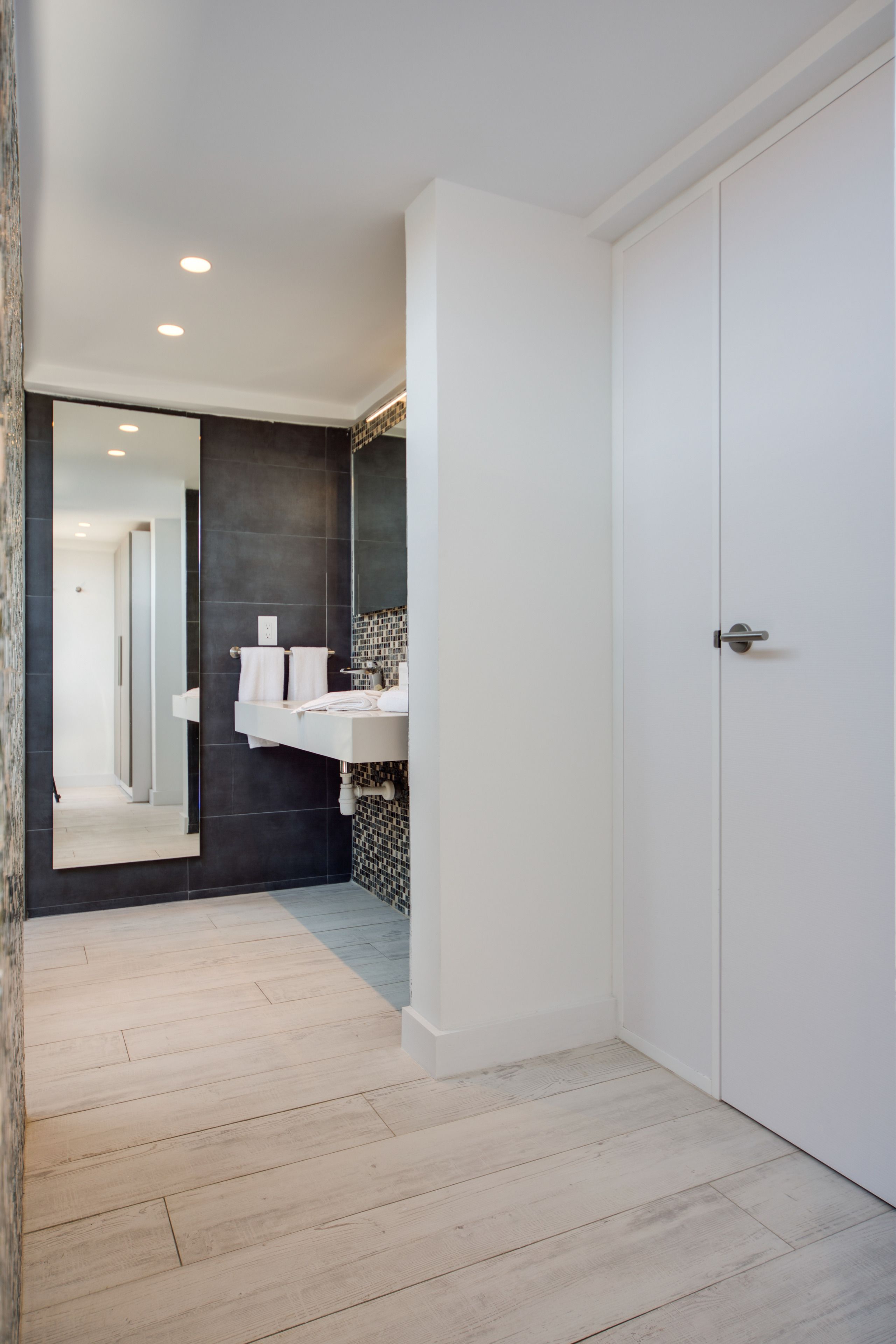 A modern bathroom with a white vanity, dark tiled backsplash, and a large mirror.