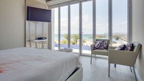 Ein Schlafzimmer mit einem großen Bett, einem an der Wand montierten Fernseher und Blick auf den Strand durch große Fenster.