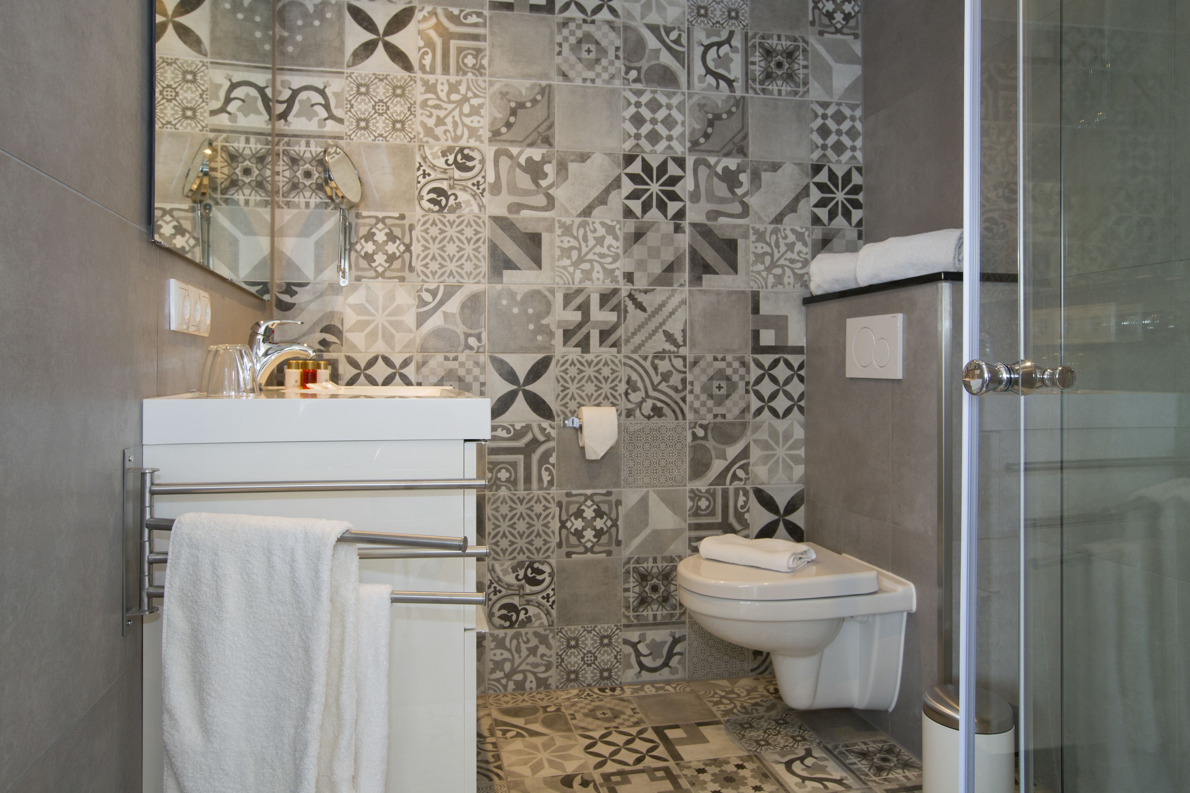 Een badkamer met betegelde spatwand, toilet, wastafel met handdoekhouder en een douchecabine met glazen wanden.