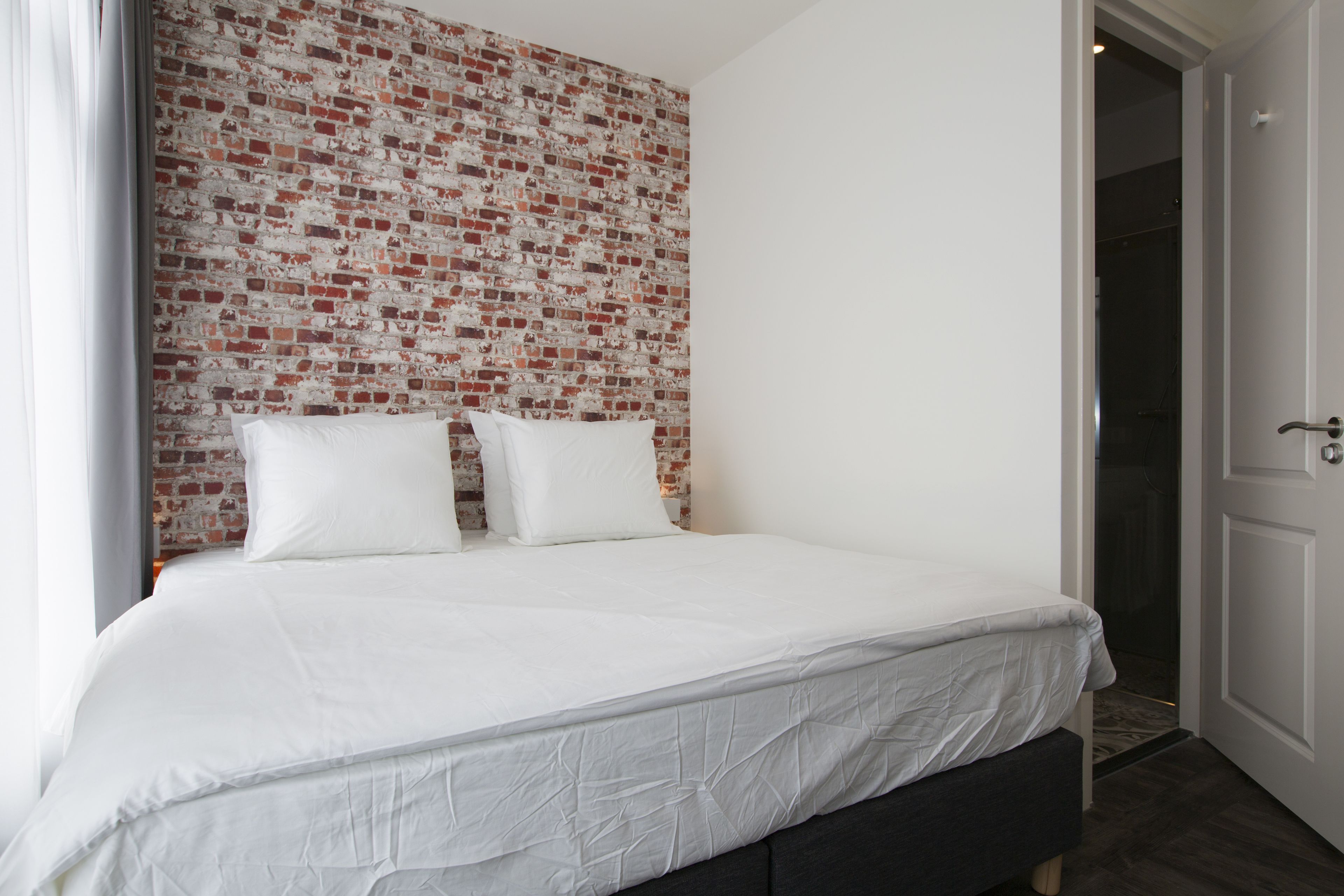 Una cama bien hecha con ropa de cama blanca en una habitación con pared de ladrillo.