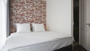 Una cama bien hecha con ropa de cama blanca en una habitación con pared de ladrillo.