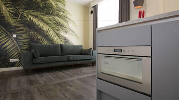 A modern kitchen with a built-in oven, a grey countertop, and a green sofa against a wall with a large leaf pattern.