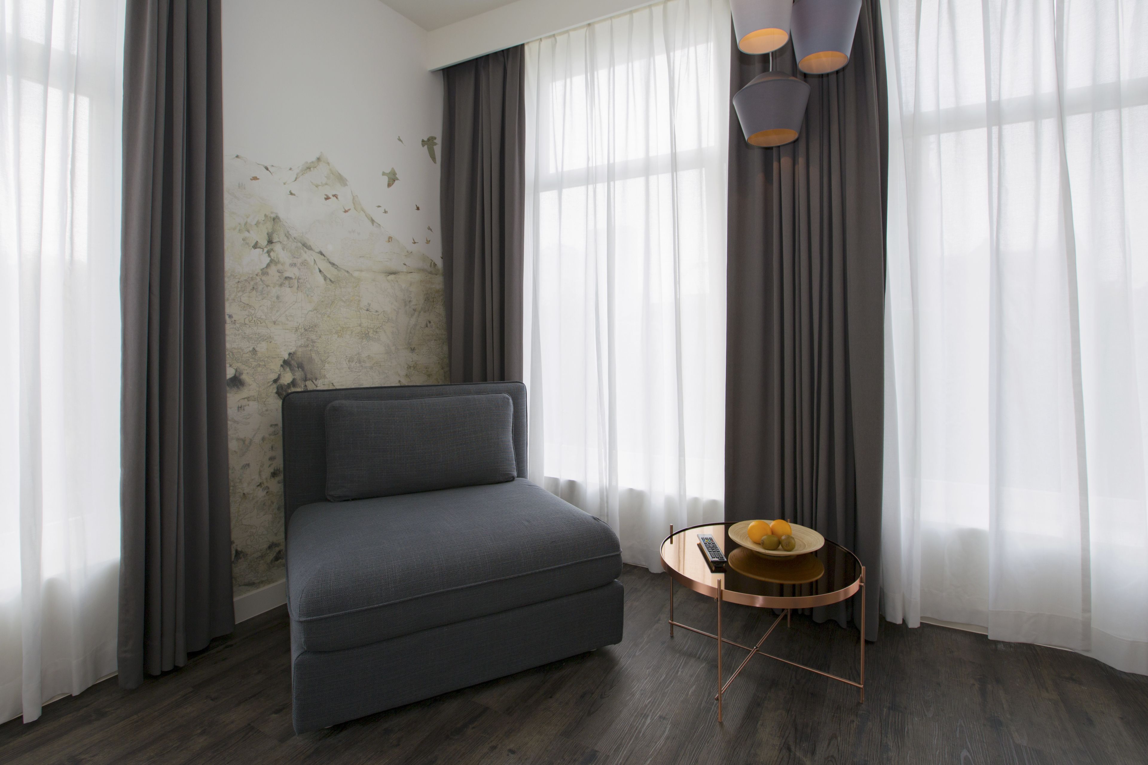 Ein modernes Wohnzimmer mit einem grauen Sofa, einem runden Couchtisch mit einer Fruchtschale und transparenten Vorhängen.