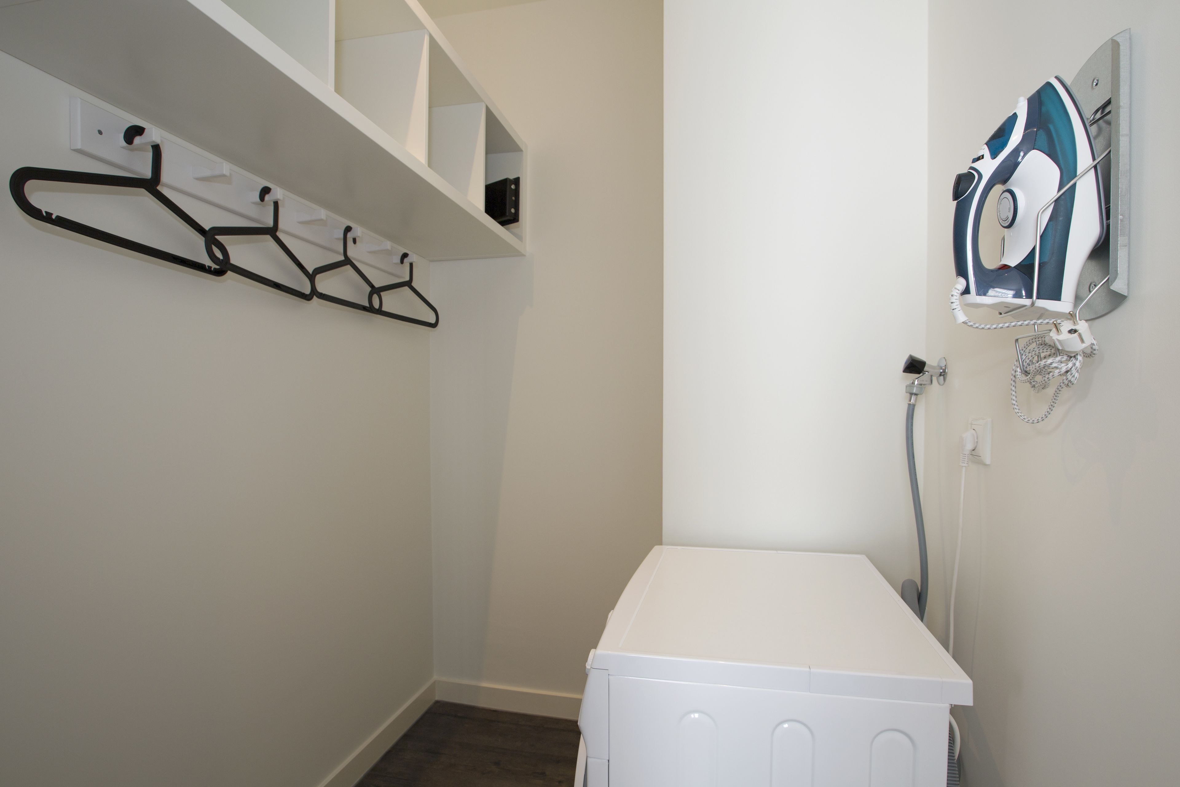 A laundry room with a white washing machine, a wall-mounted iron, and a clothes drying rack.