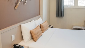 Habitación de hotel con una cama grande, mesitas de noche, una obra de arte en la pared y una ventana con cortinas.
