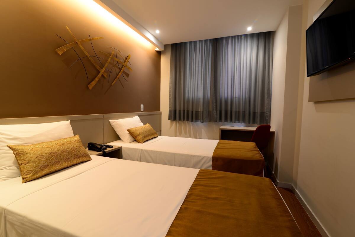 Habitación de hotel con dos camas, un escritorio, un televisor y una cortina.