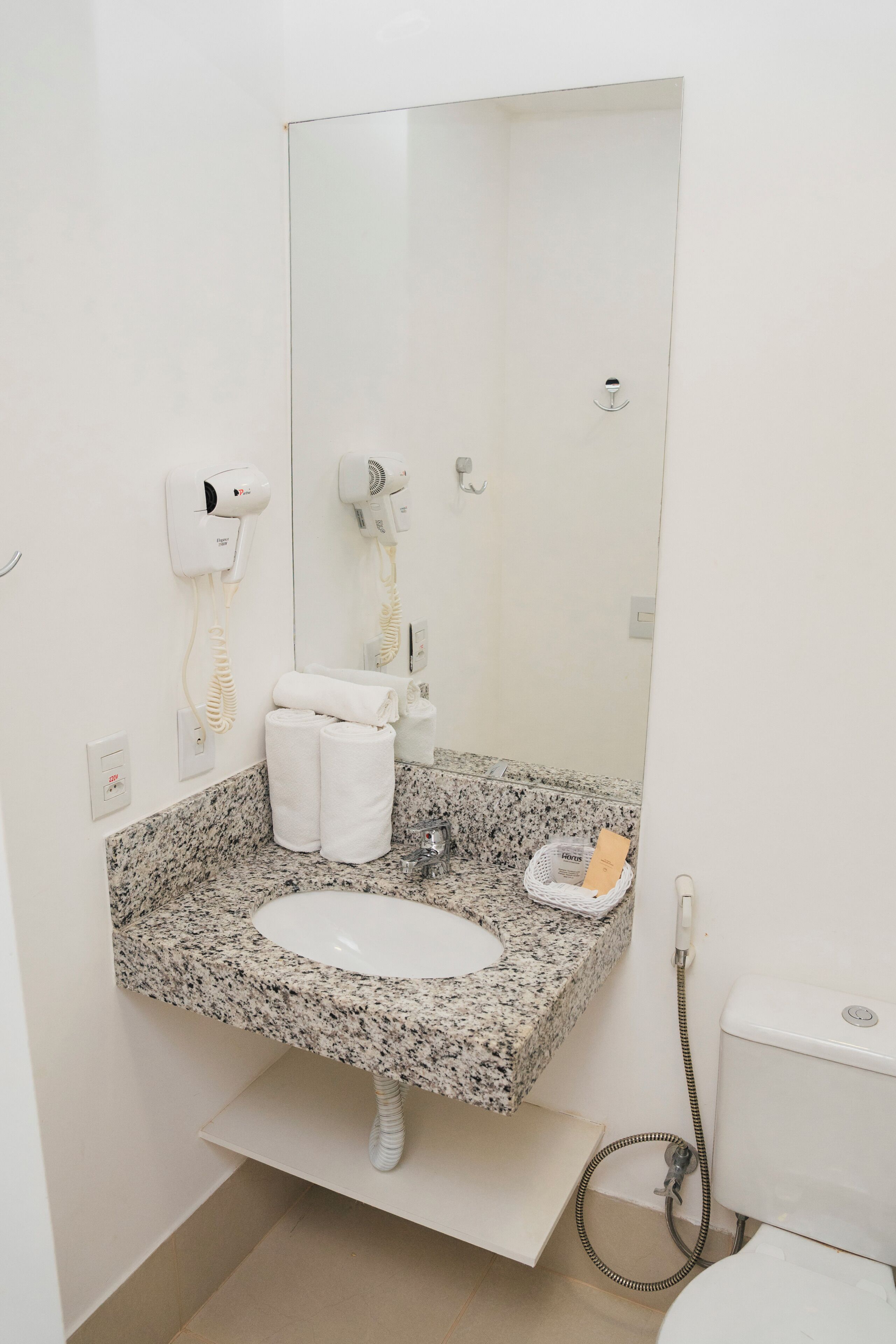 A bathroom with a granite countertop sink, a mirror, a hairdryer, a towel rack, and a toilet.