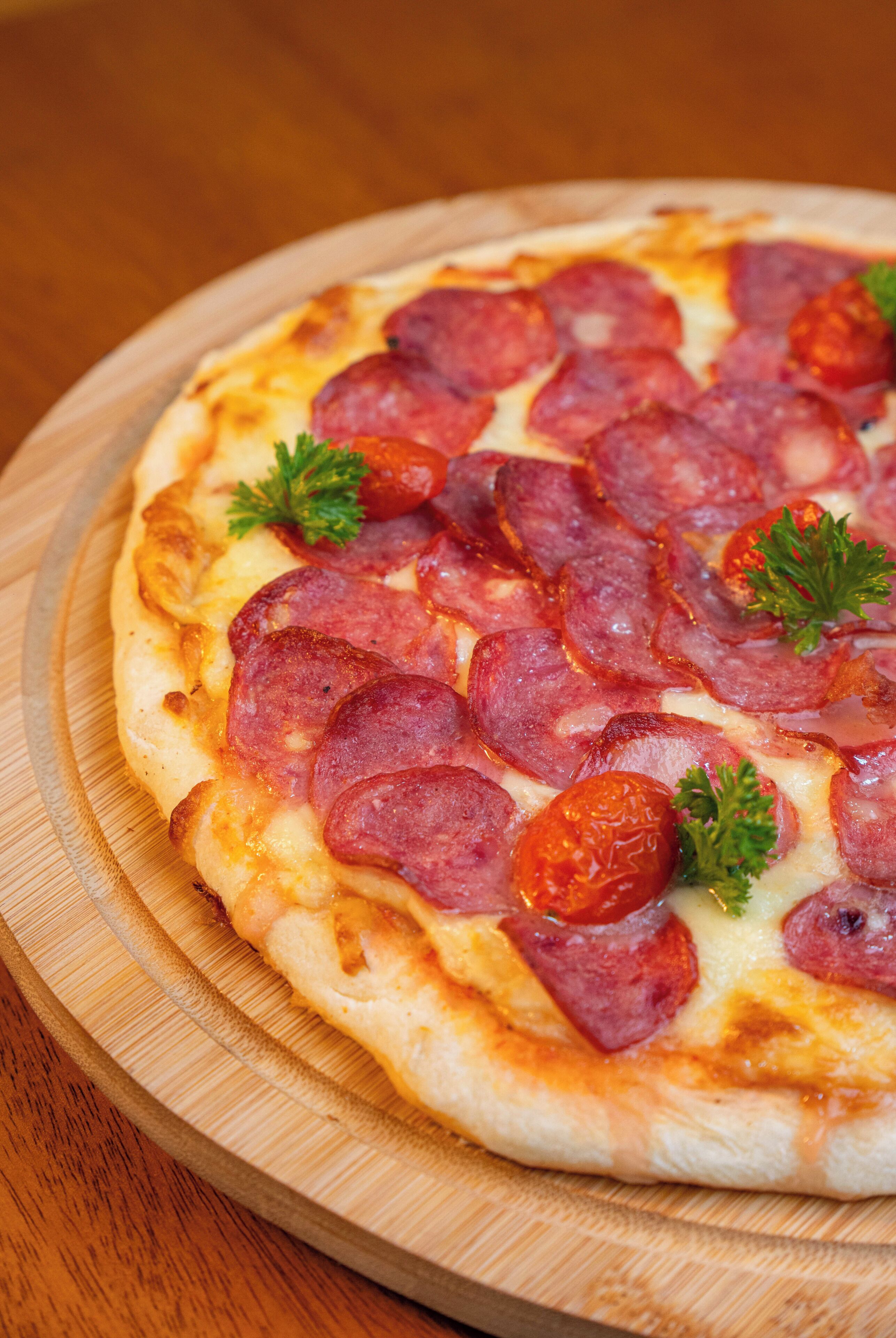 A pizza with pepperoni and parsley on a wooden board.