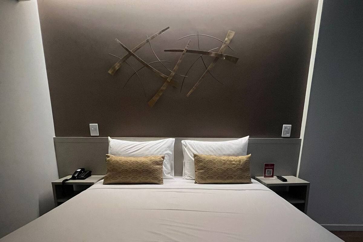 Una habitación de hotel moderna con una cama grande, dos mesitas de noche y una lámpara de pared de diseño único.