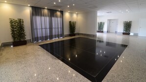 Amplia habitación con piso negro pulido, ventanas grandes con cortinas y plantas en macetas.