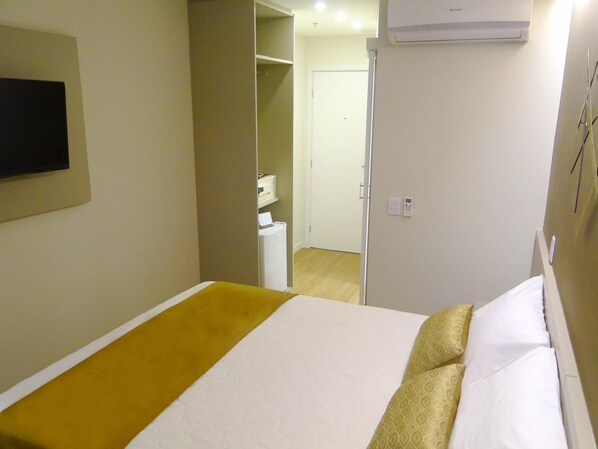 Una habitación de hotel con una cama, un televisor montado en la pared, un equipo de aire acondicionado y una puerta que da a un baño.