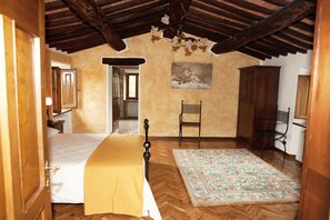 A bedroom with a bed, a chair, a rug, and a painting on the wall. - Villa di Leonardo (Sinalunga)