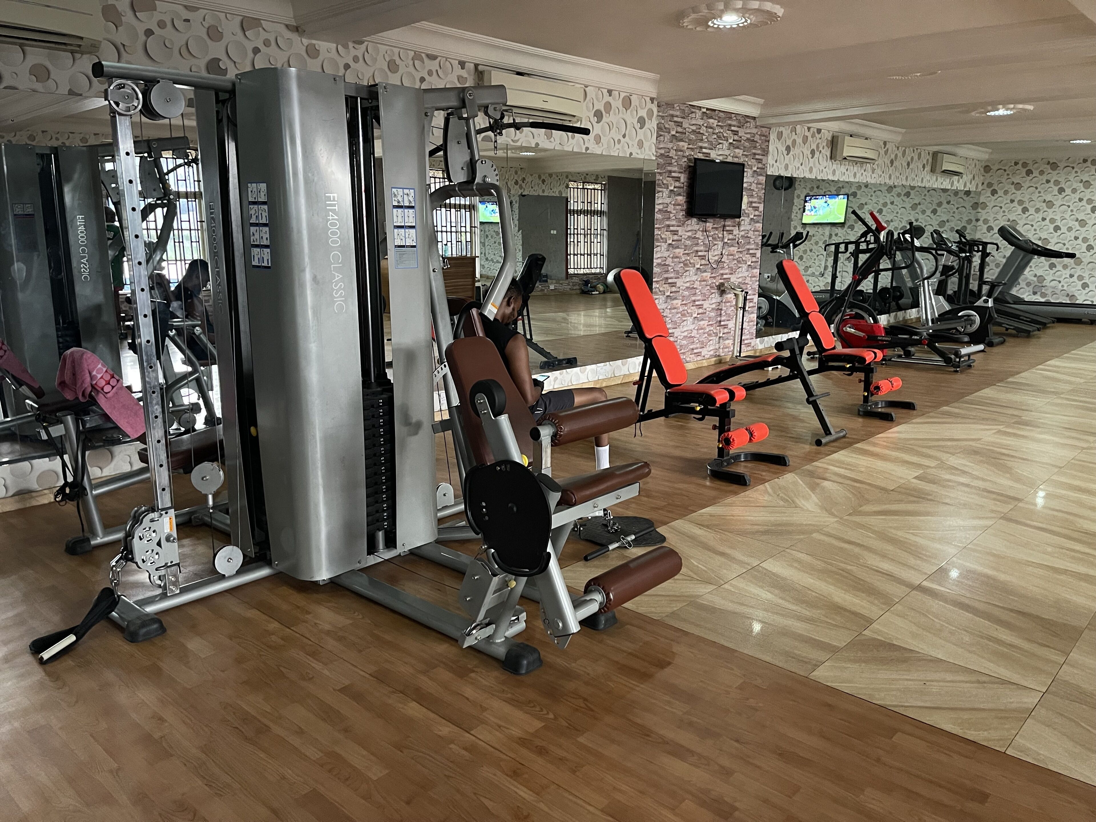 A gym with various exercise machines, a mirror, and a television on the wall.