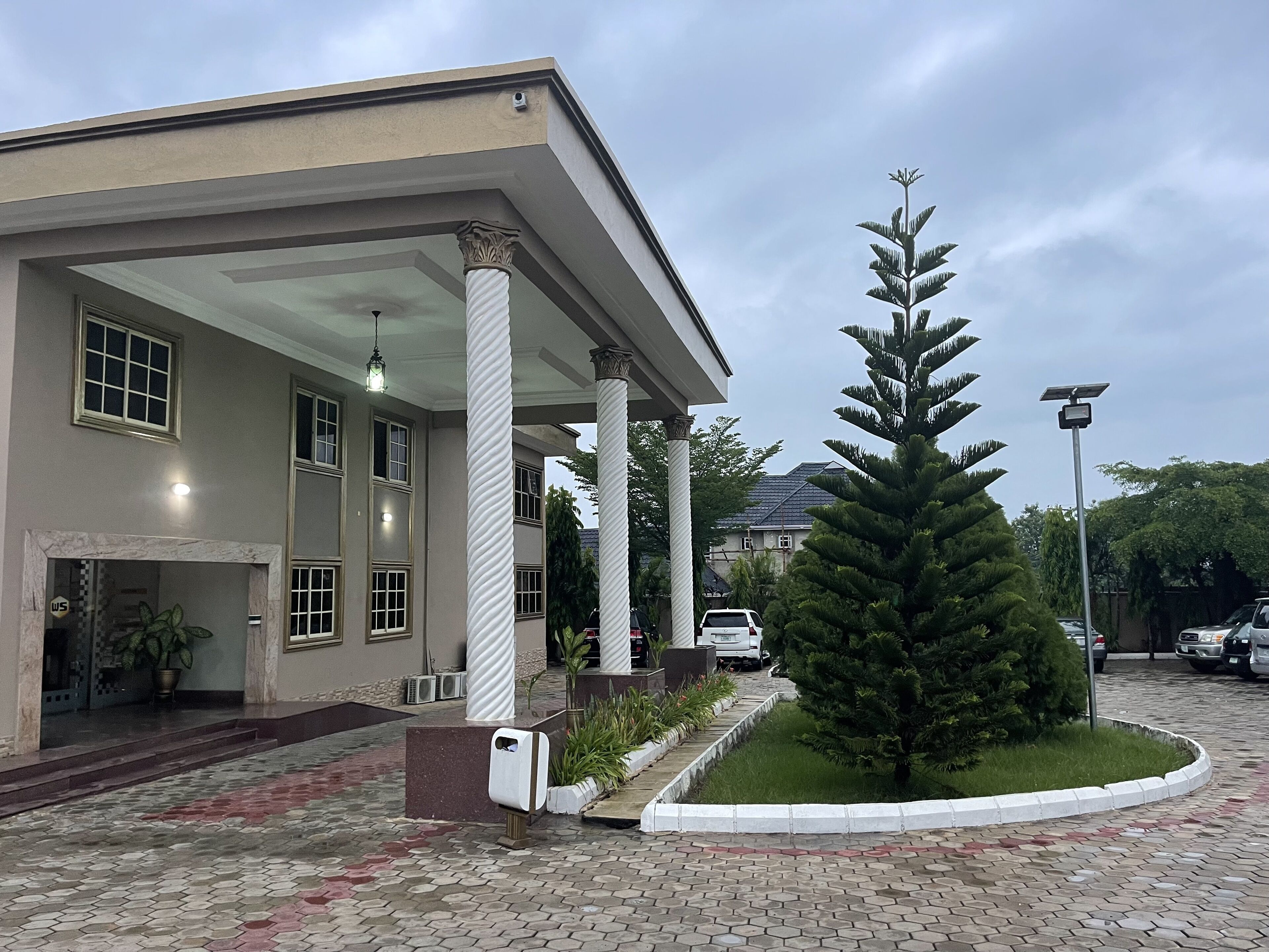 A building with a covered entrance, columns, and a small landscaped area with a tree.
