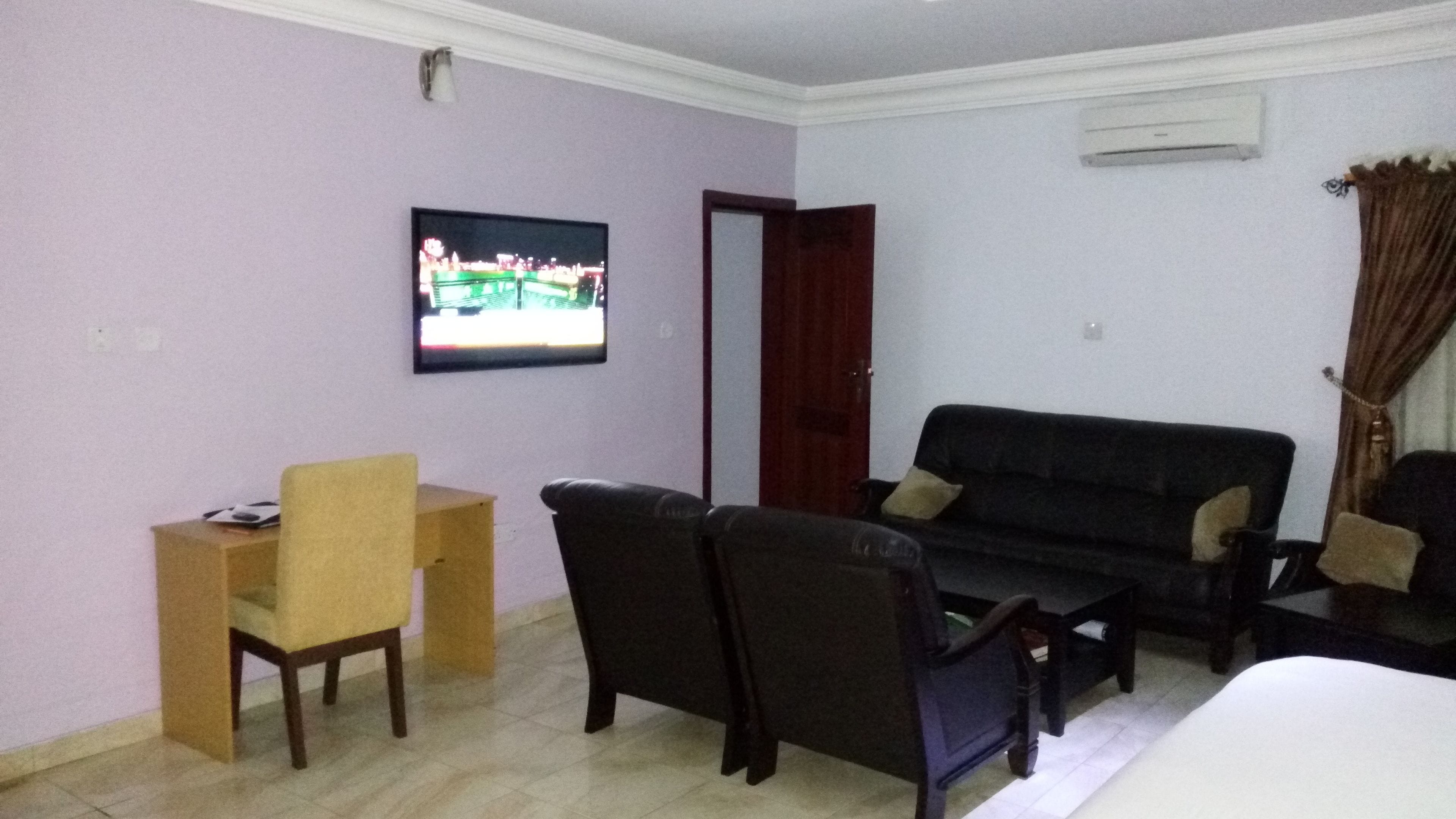 A room with a television mounted on the wall, a sofa, a chair, and a small table.