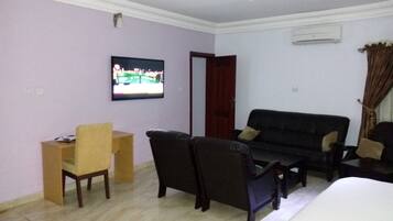 A room with a television mounted on the wall, a sofa, a chair, and a small table.