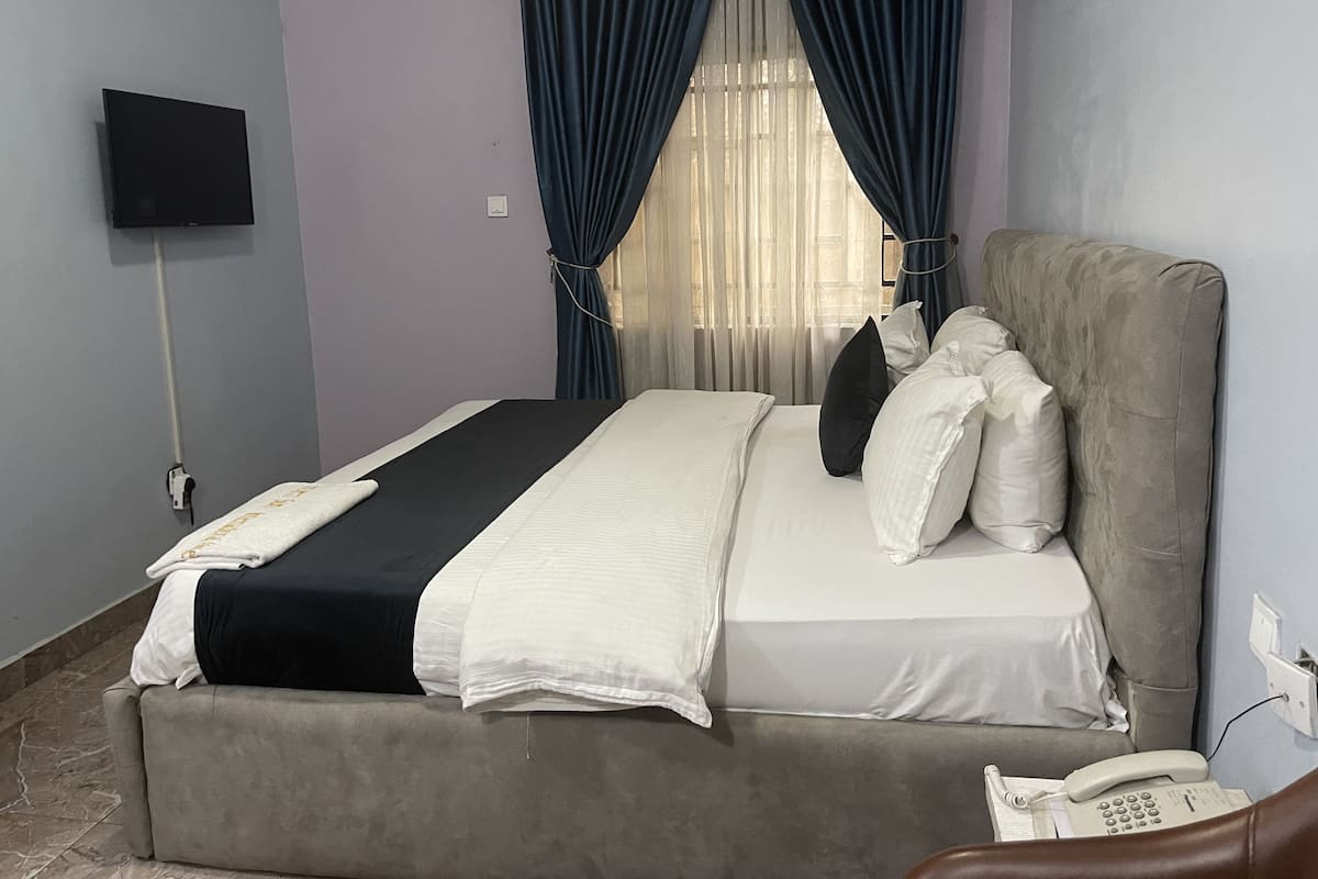 A hotel room with a bed, a TV mounted on the wall, a telephone, and a window with curtains.