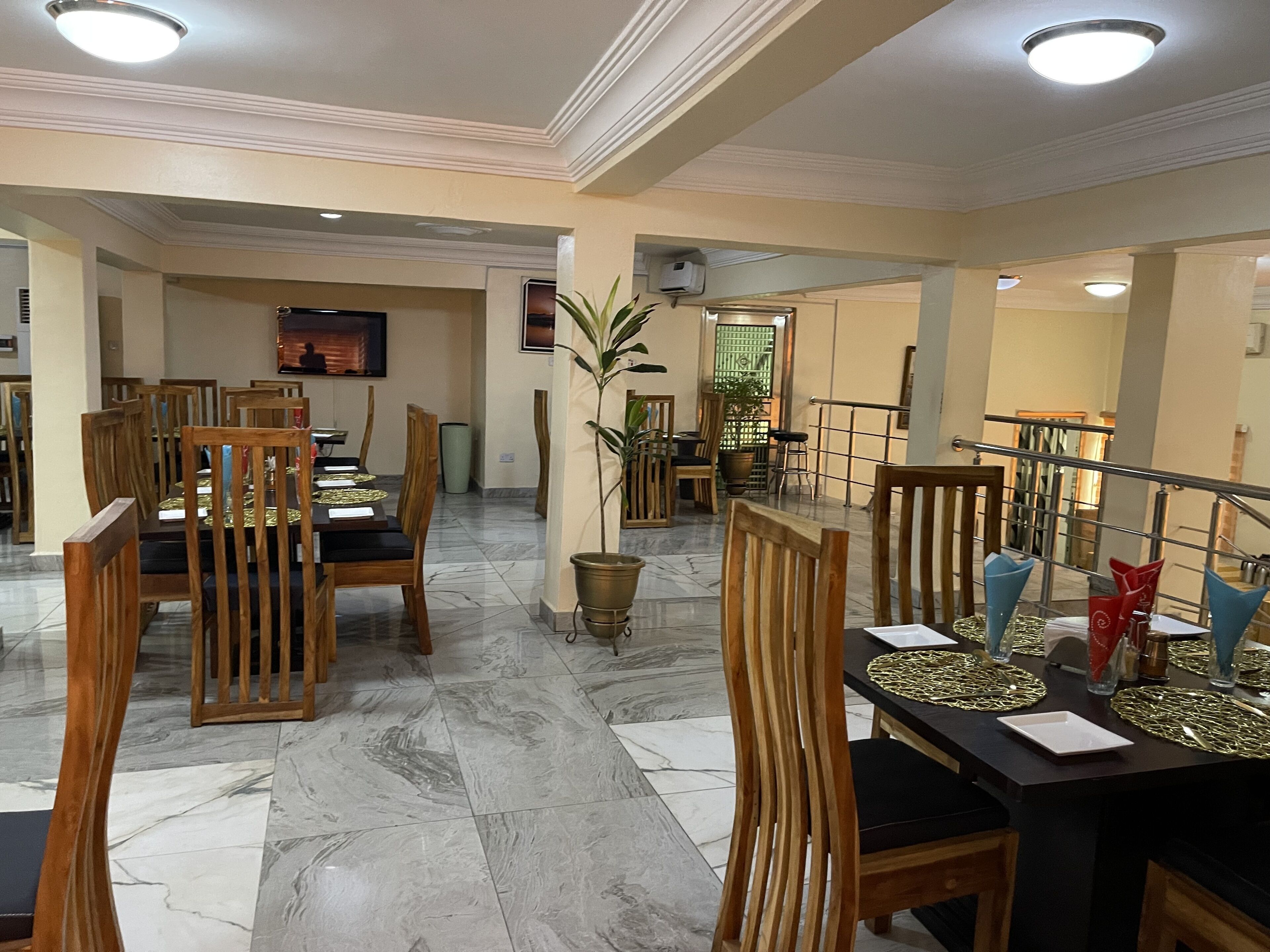 A dining area with wooden chairs and tables, marble flooring, and a potted plant.