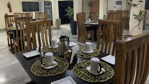 Comedor con sillas y mesas de madera, equipado con platos, tazas y cubiertos blancos.