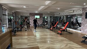 Un gimnasio con diferentes equipos de ejercicio, suelo de madera y un muro de espejos.