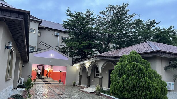 Un patio con un sendero pavimentado, un árbol grande en maceta y un edificio con entrada roja.