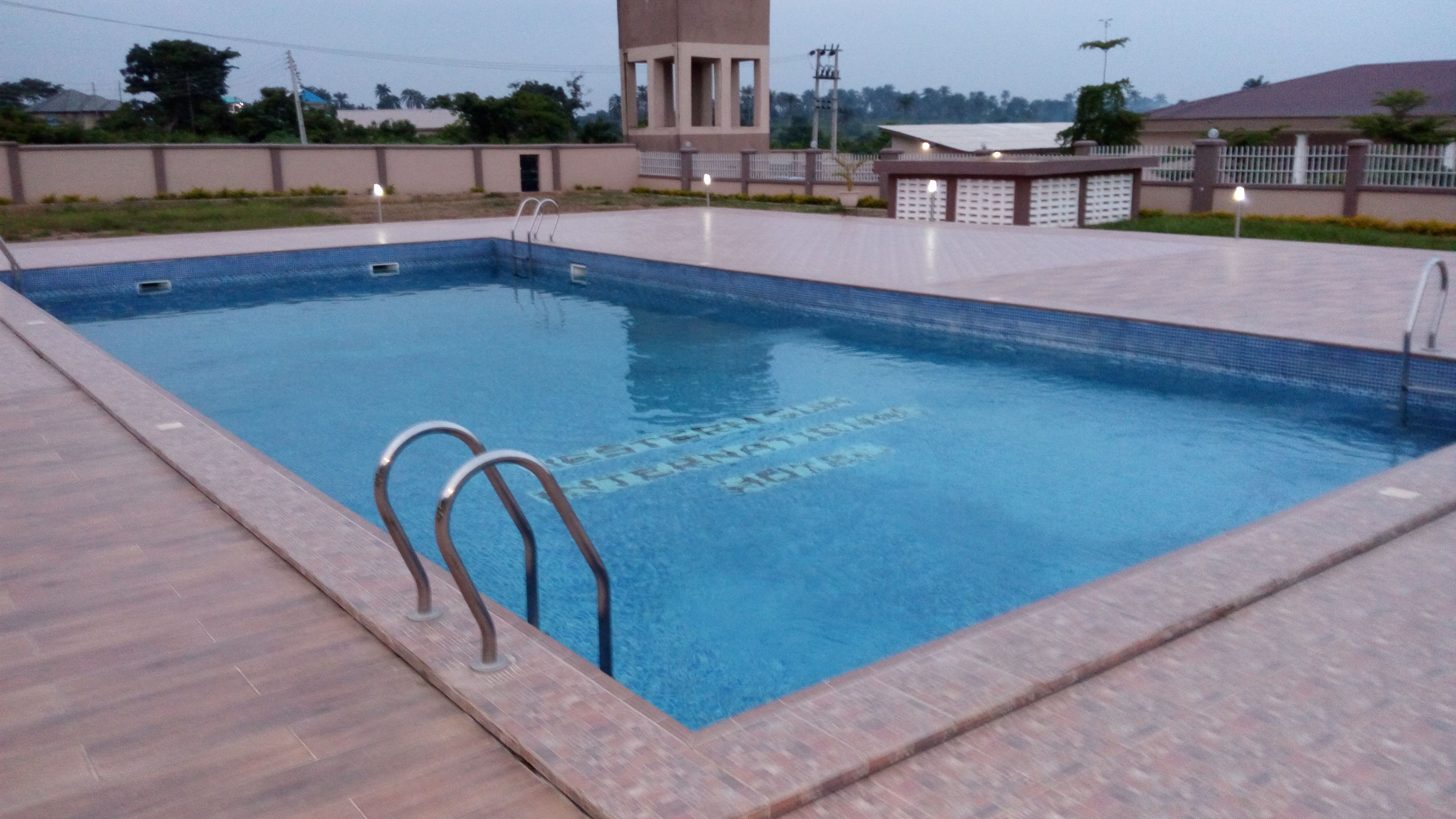 A rectangular swimming pool with a tiled edge, a ladder, and a building in the background.