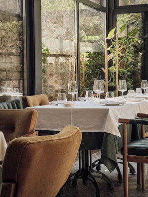 A restaurant with tables set for dining, chairs, and a view of greenery outside. - Garni Hotel Dum (Belgrade)