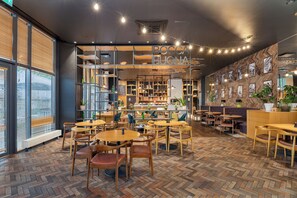 Interior de restaurante con suelo de madera en espiga, varias mesas y sillas, y un tablero de menú visible.