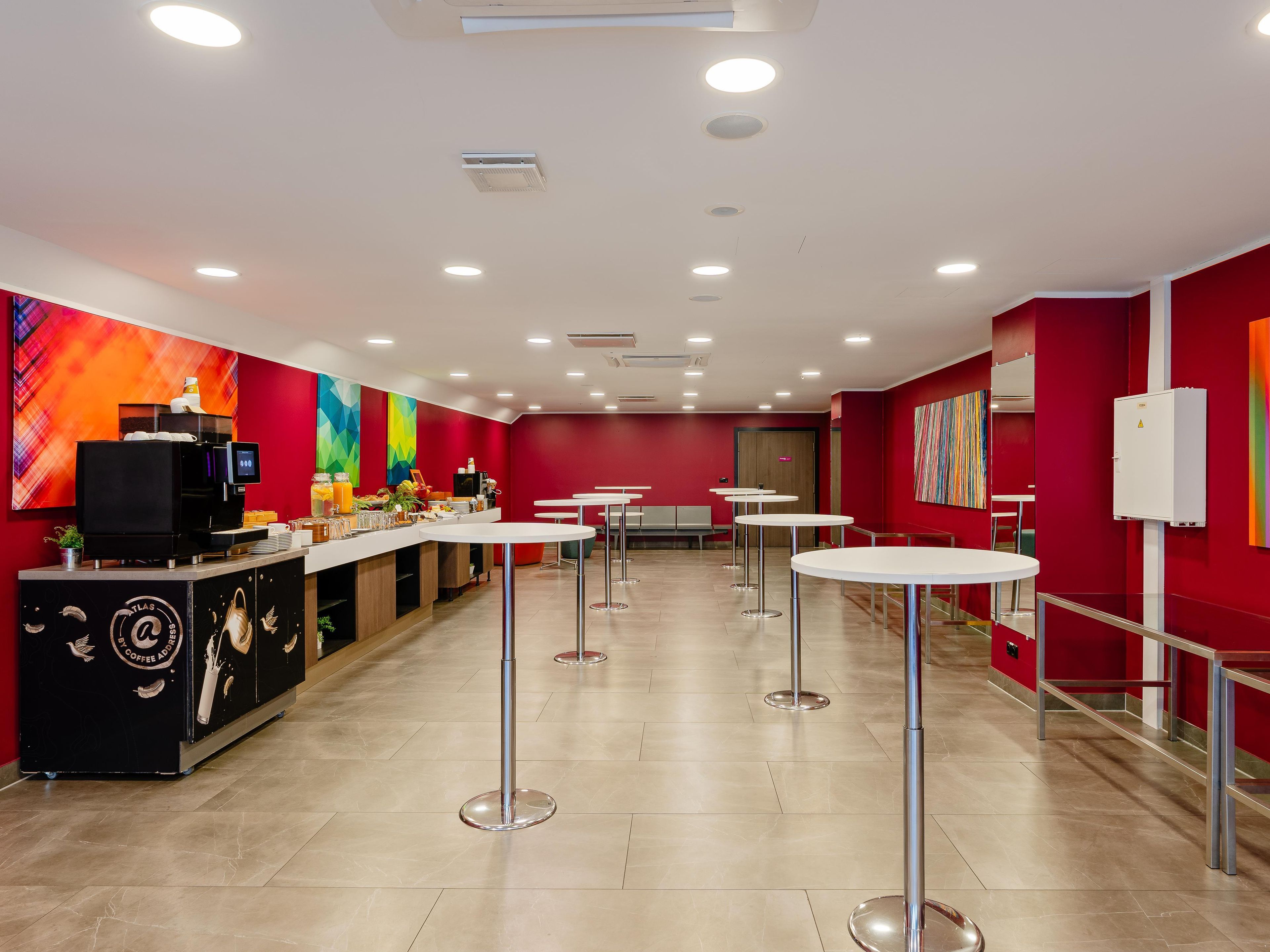 Un café moderne avec un bar à café, un espace salon et des murs rouges.