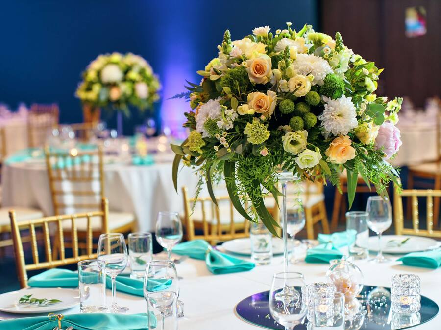 Une salle de banquet avec des tables rondes dressées pour un événement formel, agrémentée de compositions florales et de verres élégants.