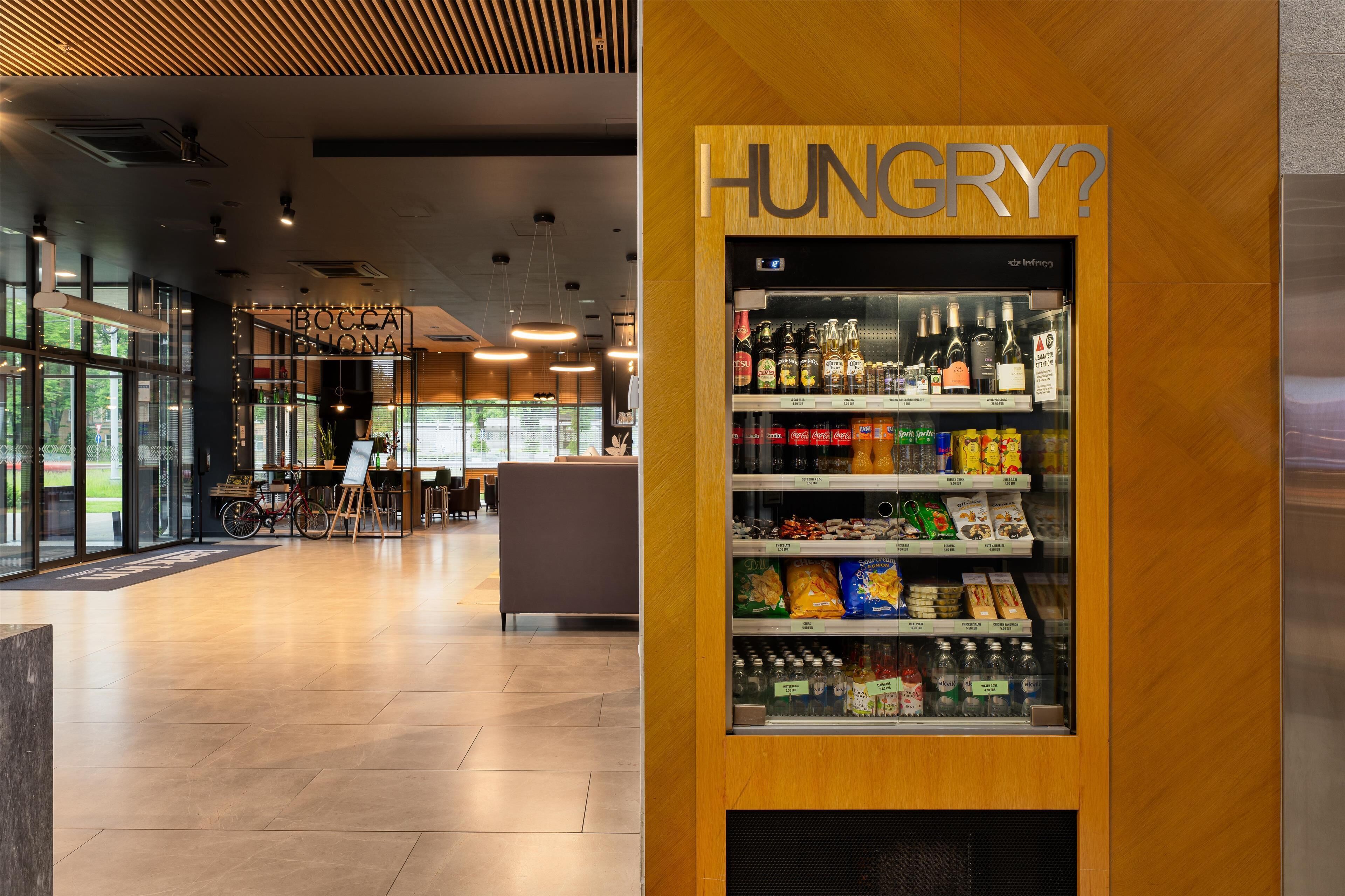Ein modernes Interieur mit einem Selbstbedienungsgetränkeautomaten mit der Aufschrift „HUNGRY?“ und einem sichtbaren Schild „BOCCA LONA“.